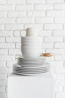 stack of white ceramic dishes and tableware on white brick wall background photo