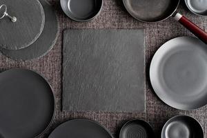 piles of black ceramic dishes and tableware top view on gray background