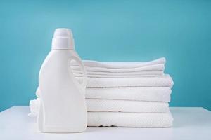 stack of clean white towels and a bottle of detergent on blue background photo