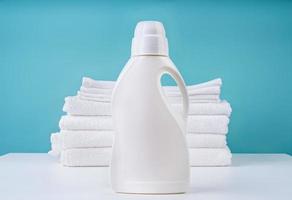 Pila de toallas blancas limpias y una botella de detergente sobre fondo azul.