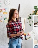 Beautiful woman artist in check shirt painting a picture at home