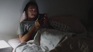 jóvenes asiáticos que usan un teléfono inteligente, navegan por la web y se desplazan por las redes sociales se alimentan en teléfonos móviles mientras están en el dormitorio. video