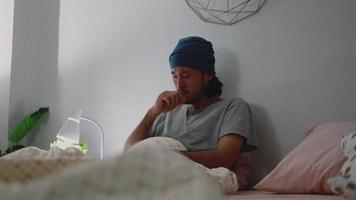 Hombre asiático tose enfermo y toma pastillas en la palma de su mano mientras está en el dormitorio de su casa.