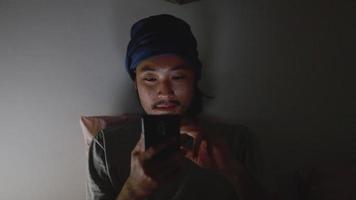 uomo asiatico che utilizza un telefono cellulare mentre giace a letto a casa a tarda notte. video