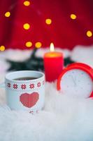 ceramic cup with red heart pattern, clock and candle with festive bokeh. happy new year. merry christmas. photo