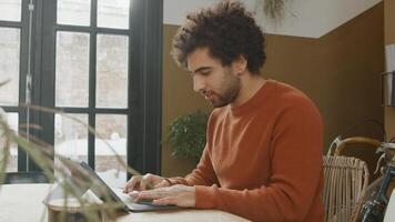 Young Middle Eastern man sits at table, typing on laptop, smiling and talking photo