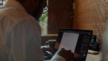 Black man wearing glasses, sitting at table, typing on laptop photo