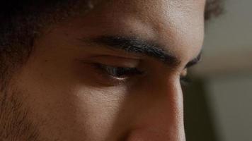 Extreme close up of face of young Middle Eastern man, looking focused, fingers touching beard