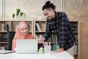 dos jóvenes colegas de la startup que son personas islámicas hablan sobre el éxito trabajando en un negocio de comercio electrónico con una sonrisa. Utilice la computadora portátil para comunicarse en línea a través de Internet en una oficina pequeña.