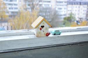 A small house stands on a balcony windowsill against a background of autumn photo