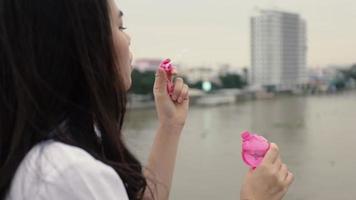 mujer asiática jugando pompas de jabón mientras está de pie en el puente.