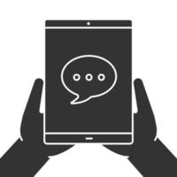 Hands holding tablet computer glyph icon. Chatting silhouette symbol. Tablet computer with speech bubble. Negative space. Vector isolated illustration