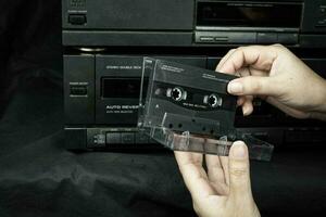 Cerrar la mano de las mujeres sosteniendo un compacto de cinta de cassette en el antiguo fondo de cinta de audio reproducida foto