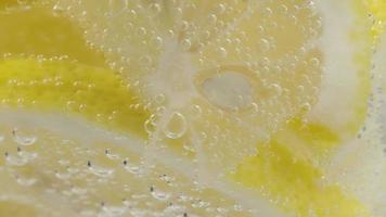 macro de rodajas de limón en bebida carbonatada con burbujas en un vaso giratorio.
