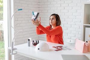 Hermosa influenciadora maestra de uñas caucásica con video chat o haciendo un blog foto