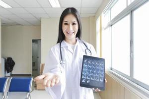 portrait of smart female doctor holding tablet to show X-Ray picture and standing at reception of the hospital. photo