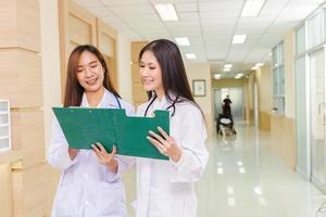 Two female doctors discussed together about a patient case with clipboard and stood at the reception of the hospital. photo