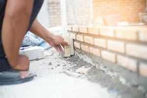 Hand pushes down brick in cement building a wall photo