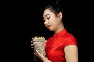 retrato, asiático, joven, mujer, vestido rojo, tradicional, cheongsam, tenencia, un, moneda de oro, en, un, saco, en, el, fondo negro foto