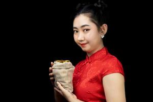 Portrait Asian young, woman red dress traditional cheongsam holding a gold coin in a sack at the black background photo