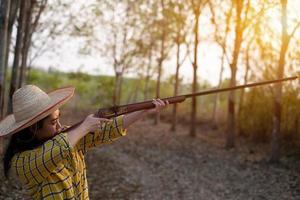 Portrait the farmer asea woman wearing a hat at the shooting range shot from a muzzle-loading vintage gun in the farm, Young girl standing in the attitude of aiming and looking through the sight rifle photo