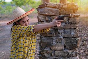 Portrait the farmer asea woman wearing a hat at the shooting shot from old revolver gun in the farm, Young girl sitting in the attitude of aiming and looking through the sight handgun photo