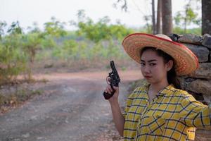 Portrait the farmer asea woman wearing a yellow Shirt hand holding old revolver gun in the farm, Young girl with a handgun in garden photo