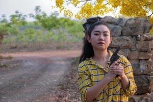 Portrait the farmer asea woman wearing a yellow shirt hand holding old revolver gun in the farm, Young girl with a handgun in garden photo