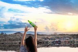 The back woman stands in hand have green glass bottle and clear plastic bottle at mountain large garbage background