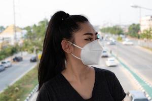Close up of a woman standing putting on a respirator N95 mask to protect from airborne respiratory diseases as the flu covid-19 coronavirus ebola PM2.5 dust and smog on the road burred background photo
