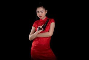 Portrait of a beautiful young Asia woman red dress traditional cheongsam holding gun at the black background photo