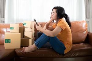 Portrait bored young Asia woman is sitting using a mobile phone on the sofa at her room photo