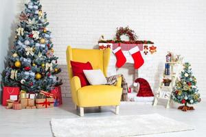 Christmas decor of bright stylish living room with yellow armchair, fireplace, Christmas tree and red candles, new year concept photo