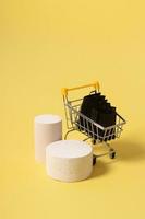Empty mock podiums or pedestals and miniature supermarket cart with shopping bags in black friday sale on yellow background photo