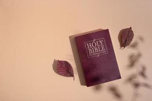 Top view Holy Bible with shadows and  autumn leaf on orange background photo