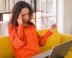 Latin woman working with laptop on sofa with tired feeling photo