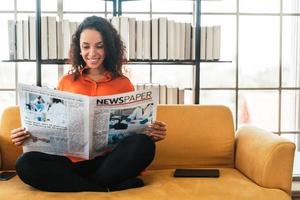 Mujer de América Latina leyendo el periódico en el sofá foto