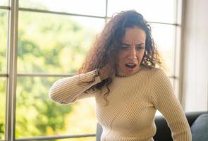 Latin woman sitting on sofa with neckache feeling photo