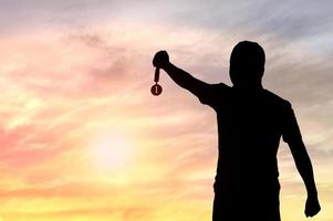 Silhouette of man holding Golden Medal on sunset background, concept as winner and champion in sport and business