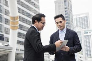 Businessman presenting work to boss, leader about planning project by laptop outside building photo