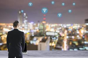 businessman use laptop on marble table with WiFi icon on blur night city background, technology and connection concept photo