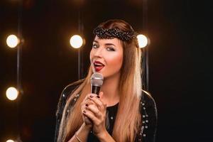 Sonriente joven hermosa chica de pelo largo con micrófono cantando una canción en el escenario de karaoke