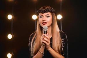 Sonriente joven hermosa chica de pelo largo con micrófono cantando una canción en el escenario de karaoke