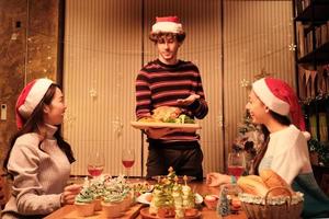 comida especial de la familia, el joven sirve pavo asado a los amigos, alegre con bebidas y disfruta comiendo, cena en el comedor de la casa decorado para el festival de navidad y la fiesta de las celebraciones de año nuevo. foto