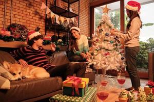Family with dog and friends together are happily decorating the white Christmas tree in the home's living room, fun and cheerful prepare for a celebration party for the New Year festival holiday. photo