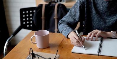 Cropped photo hand of woman writing making list taking notes in notepad working or learning online with laptop at home