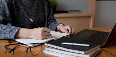 Cropped photo hand of woman writing making list taking notes in notepad working or learning online with laptop at home