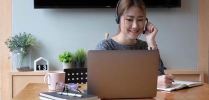 Asian student taking notes in notebook and using laptop computer for e-learning, Online learning at home concept photo