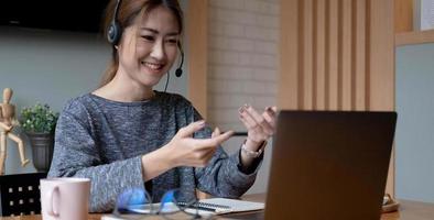 Cropped shot smiling asian woman freelancer wearing headset, communicating with client via video computer call. Millennial pleasant professional female tutor giving online language class photo