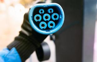 Extremo de la manguera de carga del coche eléctrico azul de siete clavijas sujetado a mano con guantes de invierno foto